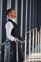 Young male passenger in elegant formal clothes is in the airport hall standing with baggage photo