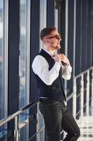 Man in elegant clothes and sunglasses is standing indoors and posing for the camera photo