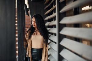 Woman with black curly hair standing near wooden windows photo