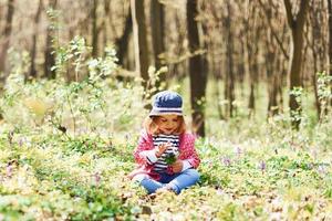 Happy little girl in blue hat have walk in spring forest at daytime photo