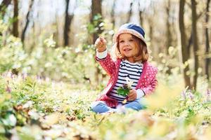 Happy little girl in blue hat have walk in spring forest at daytime photo