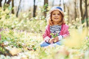 Happy little girl in blue hat have walk in spring forest at daytime photo