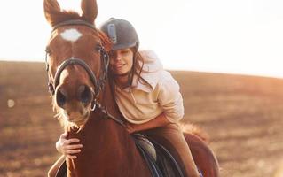 mujer joven con sombrero protector con su caballo en el campo agrícola durante el día soleado foto