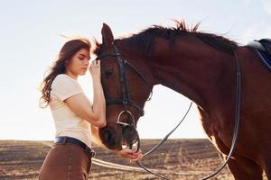 Young woman standing with her horse in agriculture field at sunny daytime photo