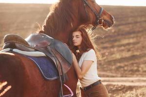 Young woman embracing her horse in agriculture field at sunny daytime photo