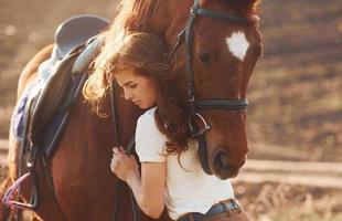 Young woman embracing her horse in agriculture field at sunny daytime photo