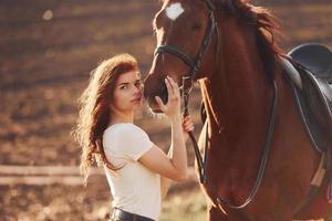 mujer joven de pie con su caballo en el campo de la agricultura en el día soleado foto