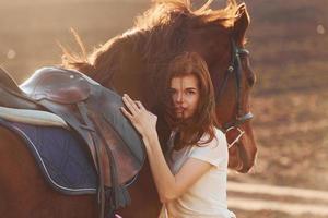 mujer joven abrazando a su caballo en el campo de la agricultura en el día soleado foto