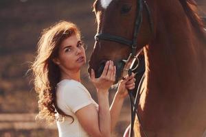 Young woman standing with her horse in agriculture field at sunny daytime photo