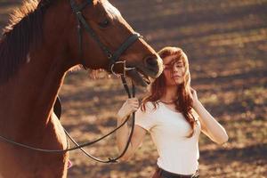 Young woman standing with her horse in agriculture field at sunny daytime photo