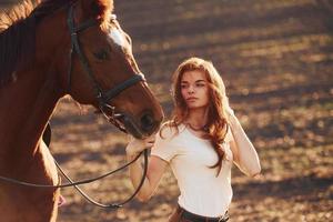 Young woman standing with her horse in agriculture field at sunny daytime photo