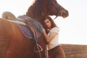 mujer joven abrazando a su caballo en el campo de la agricultura en el día soleado foto