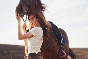 hermoso amanecer. mujer joven de pie con su caballo en el campo de la agricultura durante el día foto