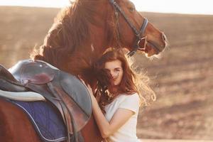 Young woman embracing her horse in agriculture field at sunny daytime photo