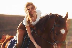 Young woman in protective hat with her horse in agriculture field at sunny daytime photo