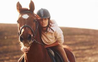 mujer joven con sombrero protector con su caballo en el campo agrícola durante el día soleado foto