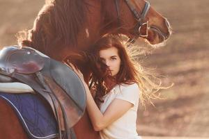 Young woman embracing her horse in agriculture field at sunny daytime photo