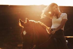 mujer joven con sombrero protector con su caballo en el campo agrícola durante el día soleado foto