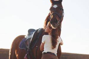 hermoso amanecer. mujer joven de pie con su caballo en el campo de la agricultura durante el día foto