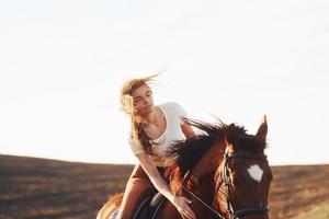 Young woman in protective hat with her horse in agriculture field at sunny daytime photo