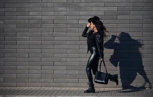 Beautiful brunette with curly hair and in black clothes have walk outdoors near wall photo