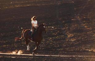 mujer joven con sombrero protector montando su caballo en el campo agrícola durante el día soleado foto