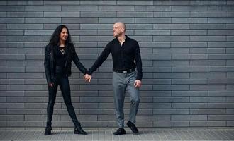 hermosa pareja vestida de negro juntos contra la pared al aire libre foto