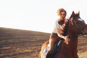 mujer joven con sombrero protector con su caballo en el campo agrícola durante el día soleado foto