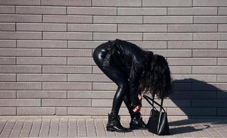 Beautiful brunette with curly hair and in black clothes have walk outdoors near wall photo