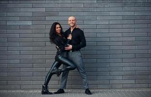 Beautiful couple in black clothes dancing together against wall outdoors photo