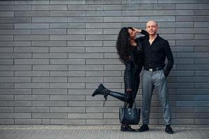 hermosa pareja vestida de negro juntos contra la pared al aire libre foto