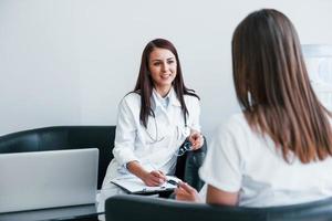 Sitting and talking. Young woman have a visit with female doctor in modern clinic photo