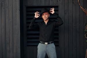 Man in black hat standing against black wooden building exterior photo