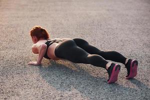 mujer en ropa deportiva haciendo flexiones en la carretera al atardecer foto