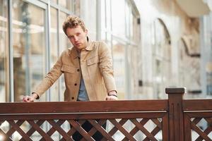 Elegant young man in formal classy clothes leaning on wooden fence outdoors in the city photo