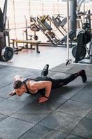 Doing push-ups. Young sportive strong man in black wear have workout day in gym photo