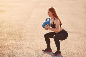 Lifting weight. Woman in sportswear have fitness day on the road at evening time photo