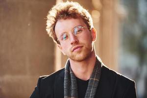 Portrait of elegant young man in glasses and formal classy clothes outdoors in the city photo