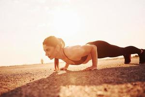 mujer en ropa deportiva haciendo flexiones en la carretera al atardecer foto