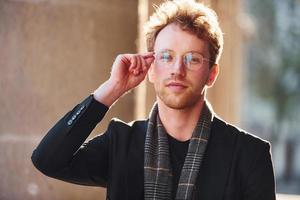 Portrait of elegant young man in glasses and formal classy clothes outdoors in the city photo