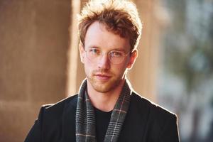 Portrait of elegant young man in glasses and formal classy clothes outdoors in the city photo