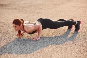 Woman in sportswear doing push-ups on the road at evening time photo