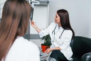 Shows results of x-ray. Young woman have a visit with female doctor in modern clinic photo