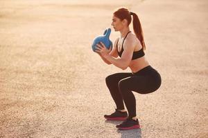 Lifting weight. Woman in sportswear have fitness day on the road at evening time photo