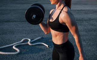 Lifting weight. Woman in sportswear have fitness day on the road at evening time photo