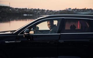 Side view of handsome unshaved man in fashionable clothes that riding his automobile photo