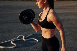 Lifting weight. Woman in sportswear have fitness day on the road at evening time photo