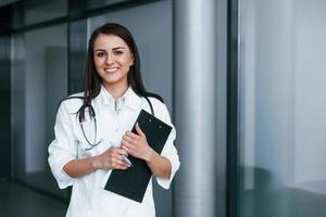 With notepad. Young nurse indoors in modern clinic. Conception of healthcare photo