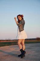 Redhead woman in skirt standing and posing for a camera on the road at evening time photo