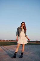 Redhead woman in skirt standing and posing for a camera on the road at evening time photo